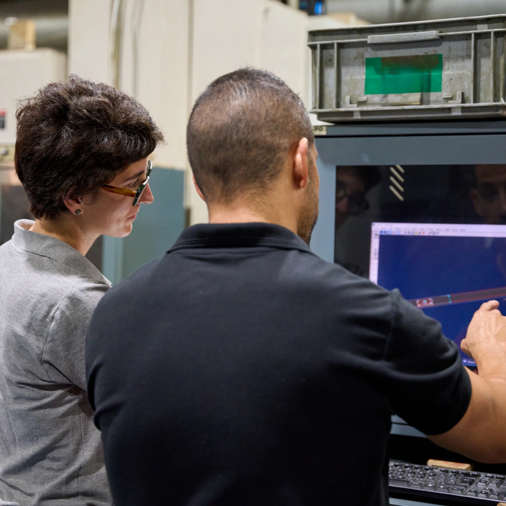 Precision Engineering Team Reviewing CNC Programming Two precision engineering team members reviewing CNC machine programming on a computer screen in a manufacturing facility.